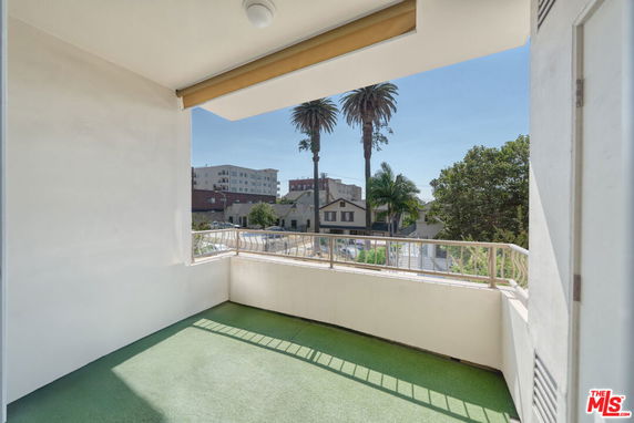 Outdoor balcony with railing offering a view of surrounding trees and buildings.
