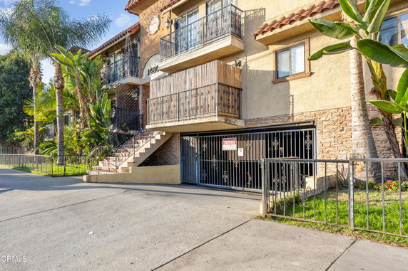 Front view of a multi-story building with balconies and gated parking area.