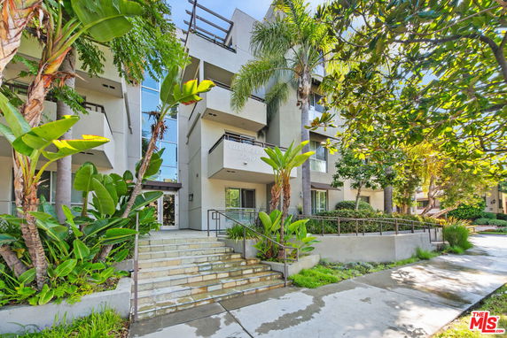 Front view of a modern multi-story apartment building with balconies and lush greenery.