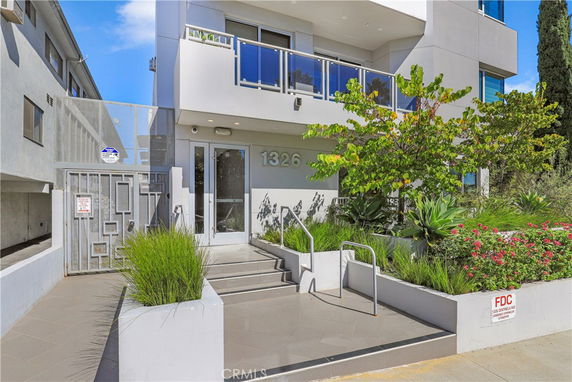 Front view of a modern multi-story building with glass balcony and landscaped entrance.