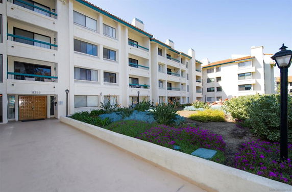 Front view of a multi-story residential building with balconies and a garden area.