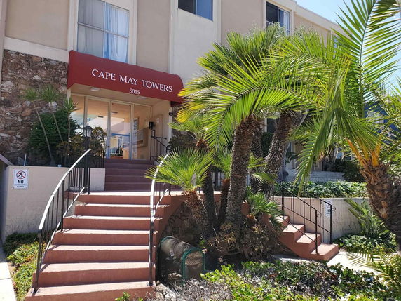 Front view of a building entrance with stairs and palm trees, featuring a sign reading Cape May Towers.