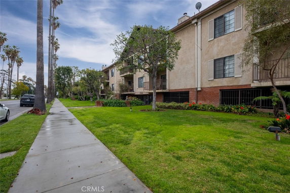 Front view of a multi-story residential building with a sidewalk and grassy area.