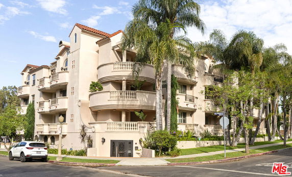 Front view of a multi-story apartment building with balconies and a tiled roof.