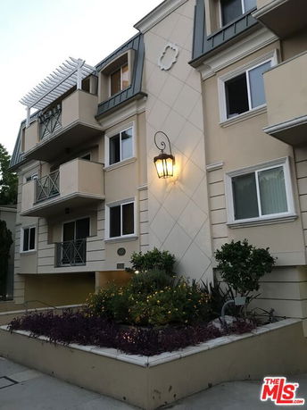 Front view of a multi-story apartment building with balconies and exterior lighting.