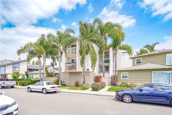 Front view of a residential building with balconies and palm trees.