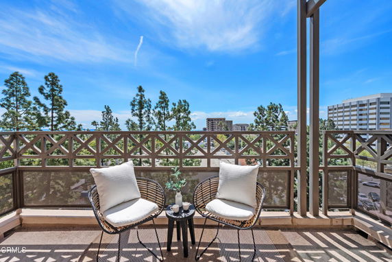 View from a balcony with outdoor chairs overlooking trees and buildings in the background.