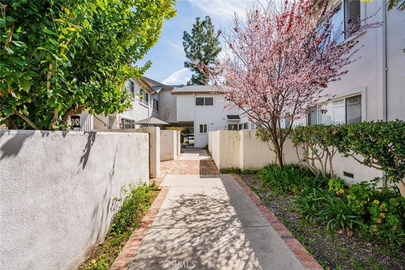 Pathway leading to the front of a two-story residential building with white walls and a small garden.