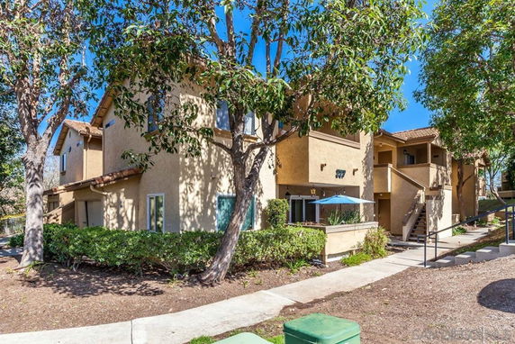 Front view of a multi-story residential building with a patio umbrella and external staircases.