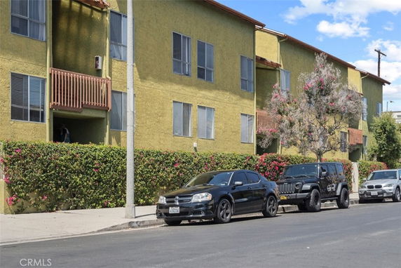 Front view of a multi-story apartment building with balconies and nearby parked cars.