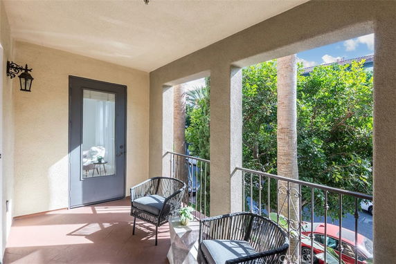 View from a covered balcony with chairs overlooking trees and a street.