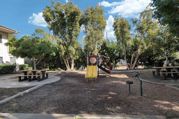 Children's play area with playground equipment and picnic tables surrounded by trees.