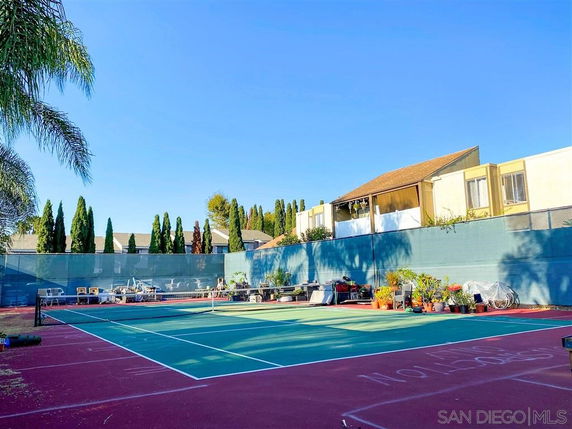 Tennis court with net and adjacent residential buildings.
