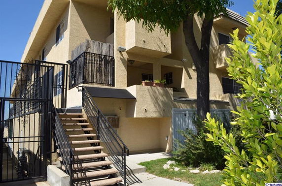 Front view of a multi-story residential building with external stairs and a gated entrance.