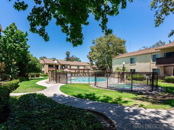 Outdoor view of a residential area with a swimming pool enclosed by a fence, surrounded by apartment buildings.