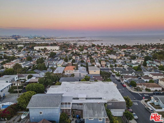 Panoramic view of suburban houses with ocean and harbor in the background at sunset.
