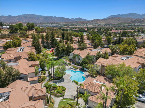 Panoramic view of a residential area with houses and a swimming pool, surrounded by trees and mountains in the background.