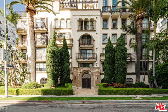 Front view of a multi-story residential building with balconies and decorative trees.