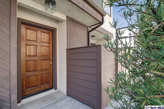 Front view of a house entrance with a wooden door and small surrounding wall.
