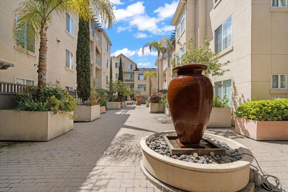View of a courtyard with apartment buildings on either side, featuring large planters and a central fountain.