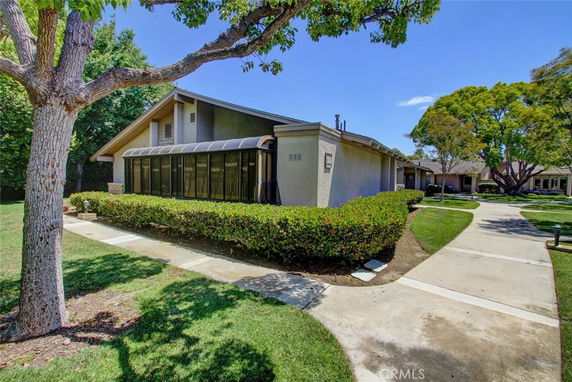 Front view of a single-story house with a sunroom and hedges along the pathway.
