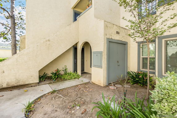 Exterior view of a beige two-story building with stairs and arched entrance.