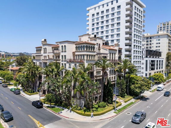 Front view of a multi-story residential building with balconies and palm trees surrounding it.