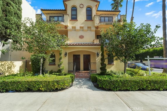 Front view of a multi-story house with balconies and decorative plants.