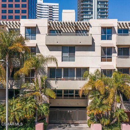 Front view of a multi-story building with balconies and palm trees in front.