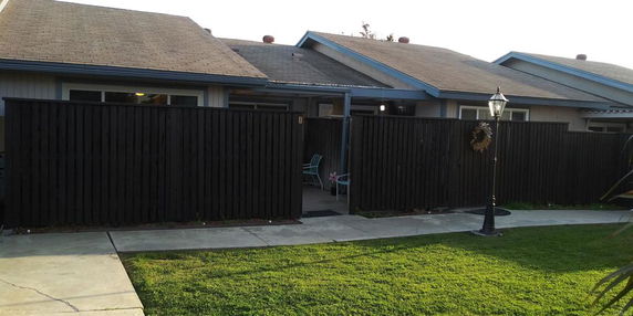 Front view of a single-story house with a fenced patio area and a lamp post.