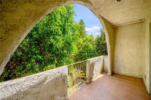 View of surrounding greenery from a covered balcony with arched opening.