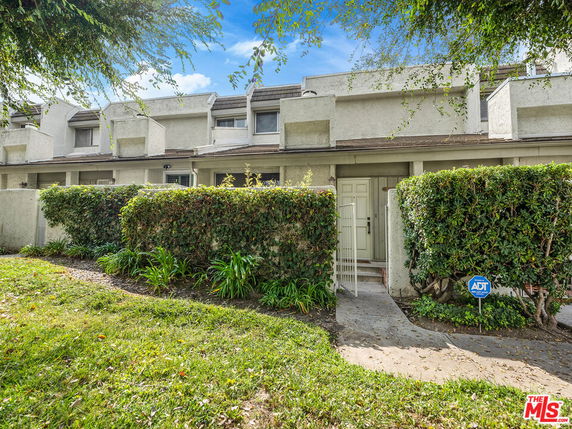 Front view of a multi-story building with hedges and a walkway.