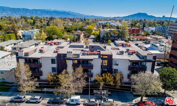Aerial view of a multi-story building with rooftop air conditioning units and a surrounding urban area.