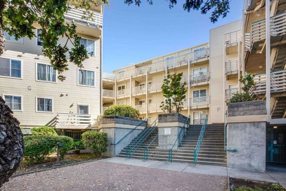 Front view of a multi-story apartment building with balconies and stairs leading to the entrance.