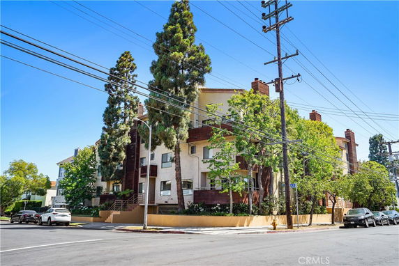 Front view of a multi-story residential building with trees and power lines.