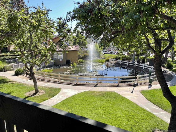 View of a garden area with a pond and fountain, surrounded by trees and pathways.