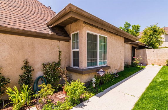 Side view of a single-story house with beige stucco walls and a sloped roof.
