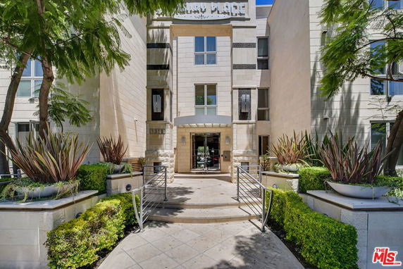 Front view of a multi-story building with an entrance ramp and decorative plants.