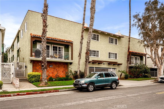 Front view of a multi-story building with balconies and palm trees in front.