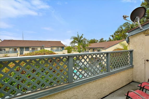 View from a balcony overlooking a residential area with a fence, rooftop, and satellite dish.