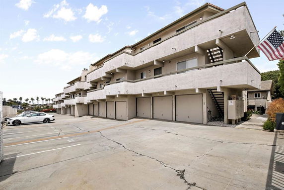 Outdoor parking area in front of a multi-story building with garages and stairs.