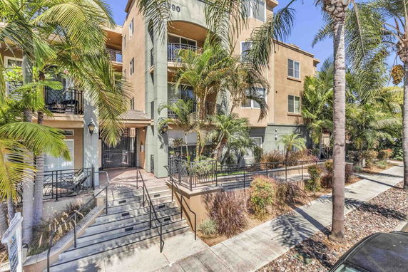 Front view of a multi-story building with balconies and surrounding palm trees.