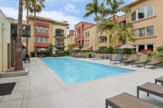 Outdoor swimming pool area surrounded by multi-story buildings and palm trees.