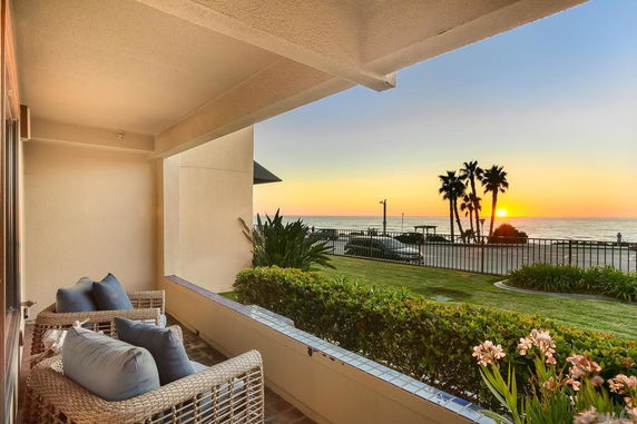 Patio area with chairs overlooking a scenic ocean view with palm trees at sunset.