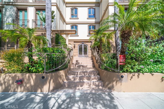 Front view of a multi-story building with decorative railings and lush greenery.