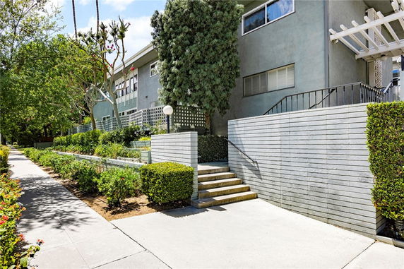 Front view of a multi-story residential building with staircase and surrounding greenery.