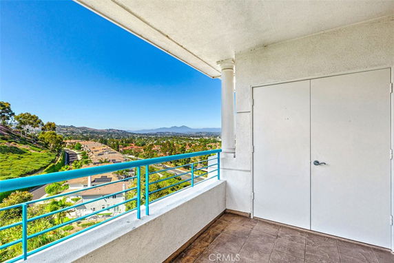 Panoramic view from a balcony with railing overlooking residential area and hills in the distance.