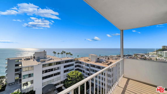 Panoramic view from a balcony overlooking the ocean and nearby buildings.