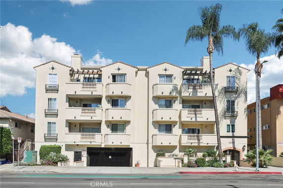 Front view of a multi-story apartment building with balconies and palm trees.