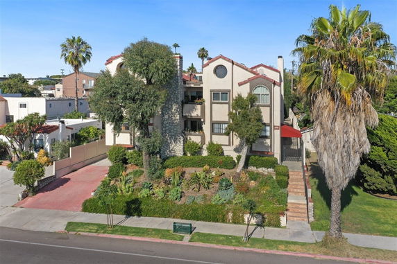 Front view of a multi-story residential building with gable roofs and a landscaped garden in front.